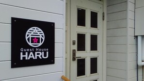 Une enseigne indiquant le nom d’une maison d’hôtes, « HARU », est fixée sur un mur blanc, à côté d’une porte blanche à six panneaux.