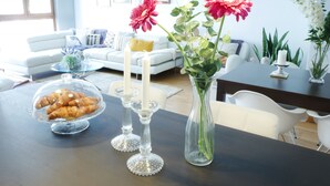 A dining table with a glass vase containing flowers, a bowl of pastries, and two candles. - Beautiful, Cosy, Great Apartment Downtown, Near Beach.  Ask for Parking. (Alicante)