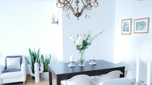 A modern dining area with a dark wooden table, white chairs, a chandelier, and a vase of white flowers. - Beautiful, Cosy, Great Apartment Downtown, Near Beach.  Ask for Parking. (Alicante)