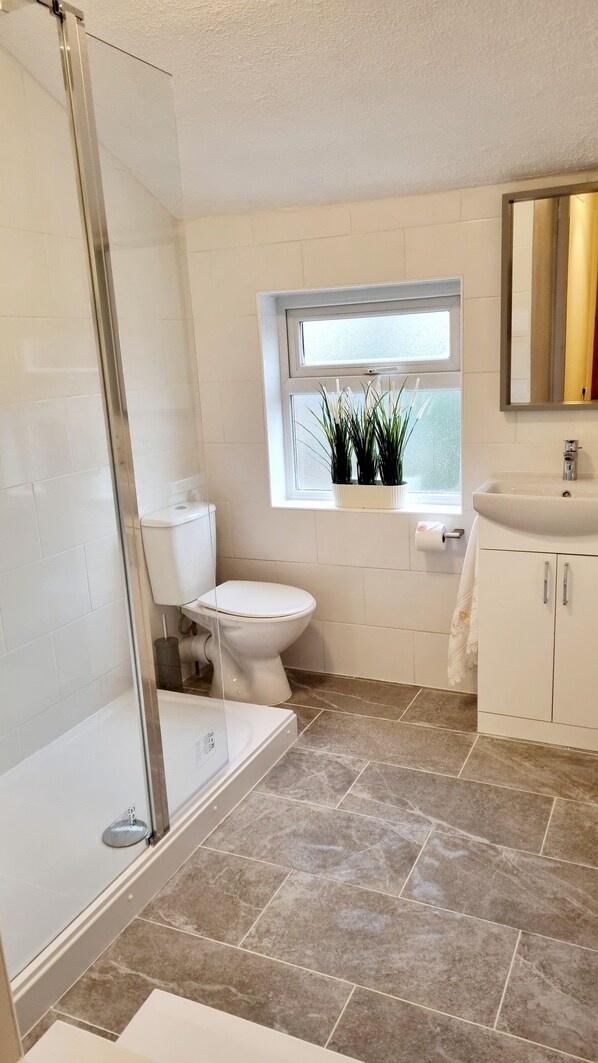A bathroom with a shower, toilet, sink, and window with plants.