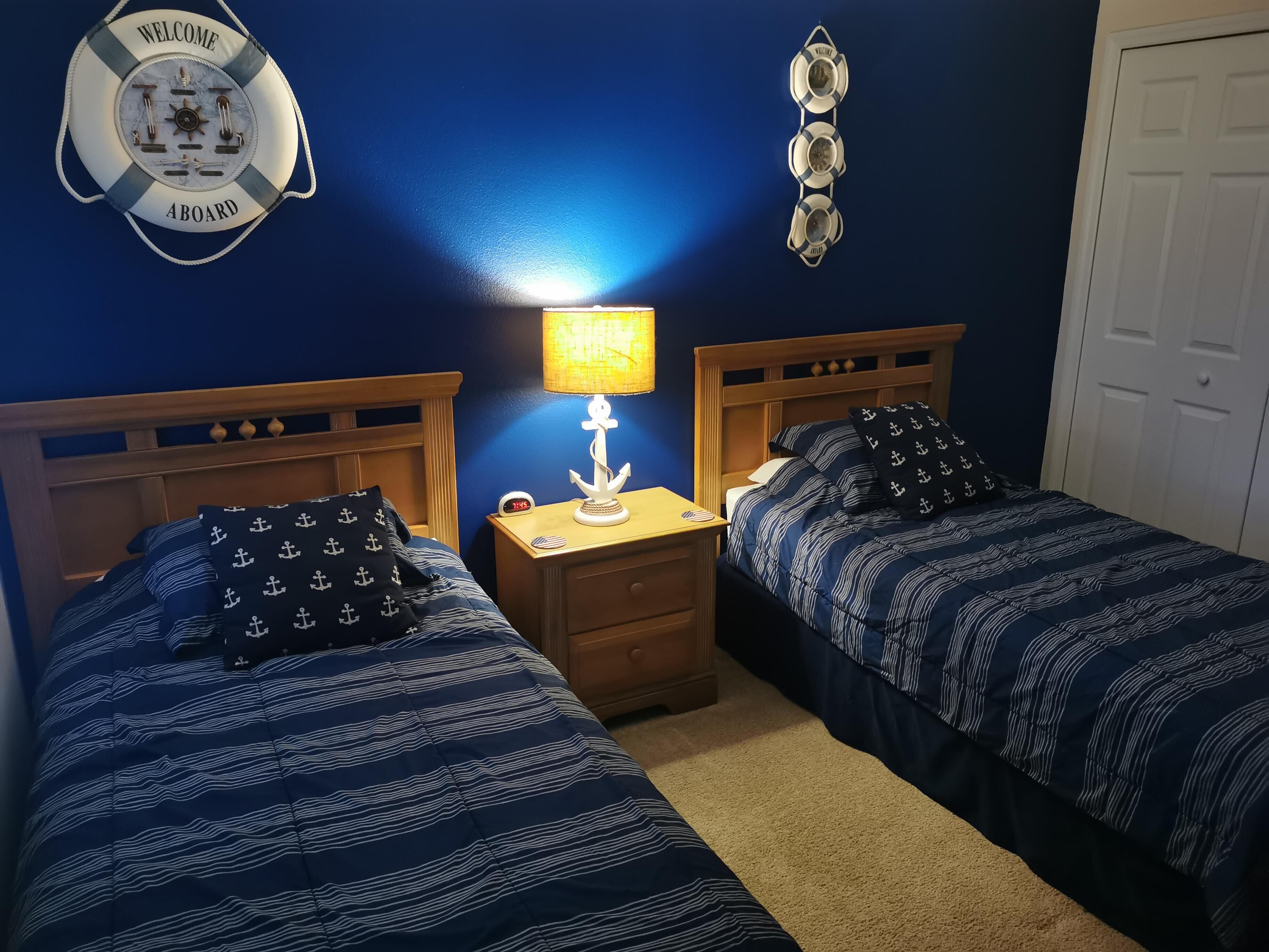 Habitación con dos camas, una mesita de noche con lámpara, un reloj de pared y decoración náutica.