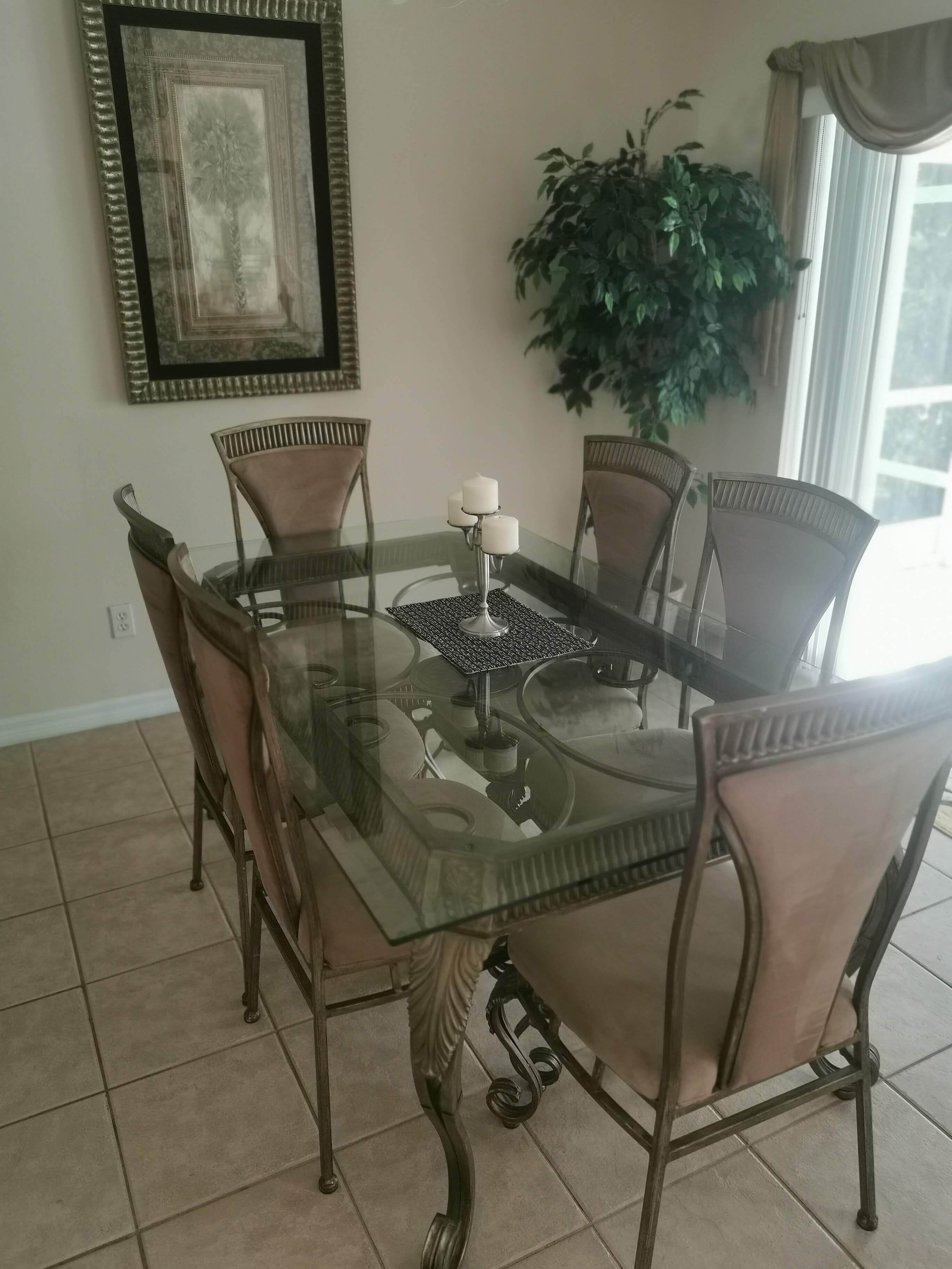 Un coin repas avec une table en verre entourée de chaises rembourrées, une œuvre d’art encadrée au mur et une plante en pot.