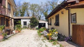 A courtyard with a gravel path, surrounded by potted plants and flowers, leading to a building with a balcony and a wooden fence. - Domus Anghelos ... in the Roman countryside (Roma)