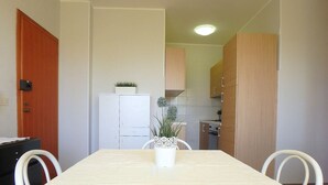 A small, compact kitchen with white cabinets, a white refrigerator, and a dining table with chairs. - three-room apartment in a beachfront condo with a view of the pedestrian walkway (Comacchio)