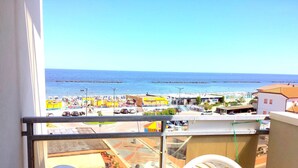 A balcony with a view of a beachside area, including a parking lot and buildings with beach umbrellas. - three-room apartment in a beachfront condo with a view of the pedestrian walkway (Comacchio)