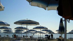 A beach with multiple umbrellas and lounge chairs, indicating a beachside resort setting. - three-room apartment in a beachfront condo with a view of the pedestrian walkway (Comacchio)
