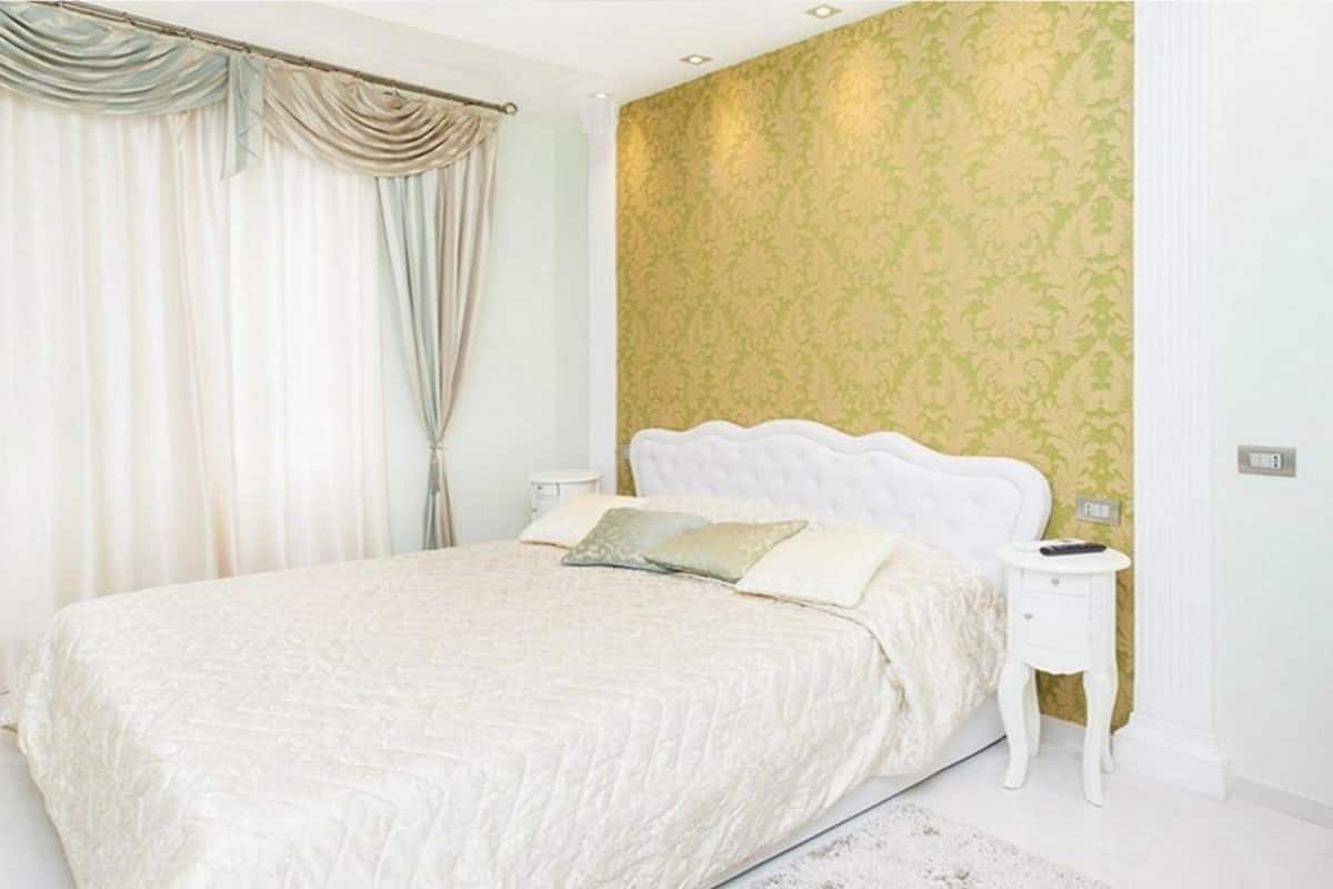 A bedroom with a large bed, a nightstand, and a wall with a patterned wallpaper.