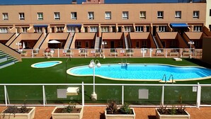 Um hotel com várias varandas, piscina central e área de gramado verde.