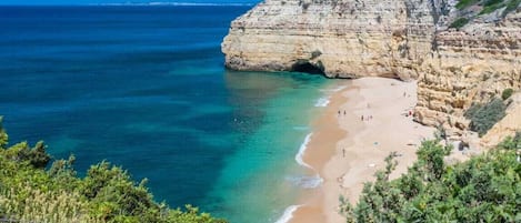 Un paysage côtier avec une plage, des falaises et une mer d’un bleu limpide.