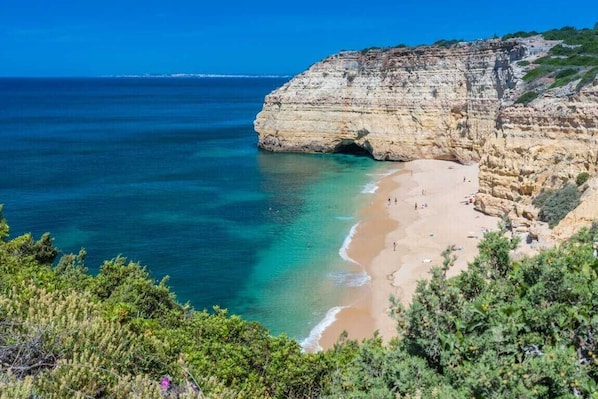 A coastal landscape with a beach, cliffs, and clear blue sea.