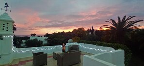 Une terrasse sur le toit, dotée d’un espace extérieur aménagé, d’une lampe décorative et offrant une vue sur le coucher de soleil.