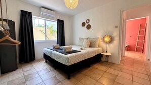 Ein Schlafzimmer mit einem Bett, einem Nachttisch, einer Hängeleuchte und Blick ins Freie durch ein Fenster.