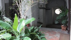 An indoor courtyard with potted plants, a tiled floor, and a stone wall. - Luxurious apartment in an ancient noble palace in the historic center of Naples (Napoli)