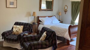 A cozy bedroom with a large bed, a smaller sofa, a wooden chair, and a nightstand with a lamp. - Charming Rural Farmhouse Cottage (by Carnwath)