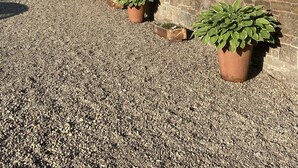 A stone building with a gravel courtyard, potted plants, and hanging flower baskets. - Charming Rural Farmhouse Cottage (by Carnwath)