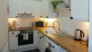 A compact kitchen with white cabinets, a microwave, an oven, a sink, and a kettle. - Charming Rural Farmhouse Cottage (by Carnwath)