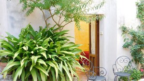 A patio with a large potted plant, a metal chair, and a small table. - Liberty apartment (Erice)