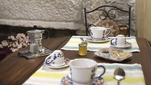 A dining table set with tea cups, saucers, a teapot, a sugar bowl, and a spoon, placed on a striped tablecloth. - Liberty apartment (Erice)