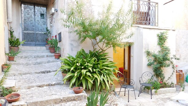 A narrow stone staircase leading to a door, surrounded by potted plants and outdoor furniture. - Liberty apartment (Erice)