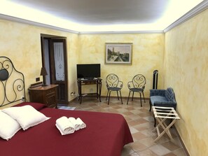 A hotel room with a bed, a desk with a TV, two chairs, a blue sofa, and a small table with a lamp. - Liberty apartment (Erice)