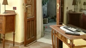 A room with a wooden door, a small table with a remote control, and a lamp on a wooden cabinet. - Liberty apartment (Erice)