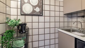 Uma cozinha com painel de azulejos, uma pia e um regador verde sobre um suporte.