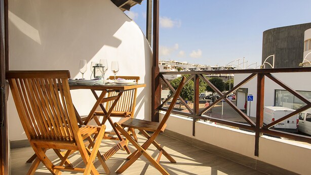Ein Balkon mit Holzmöbeln, einem Tisch und Blick auf die Stadt.