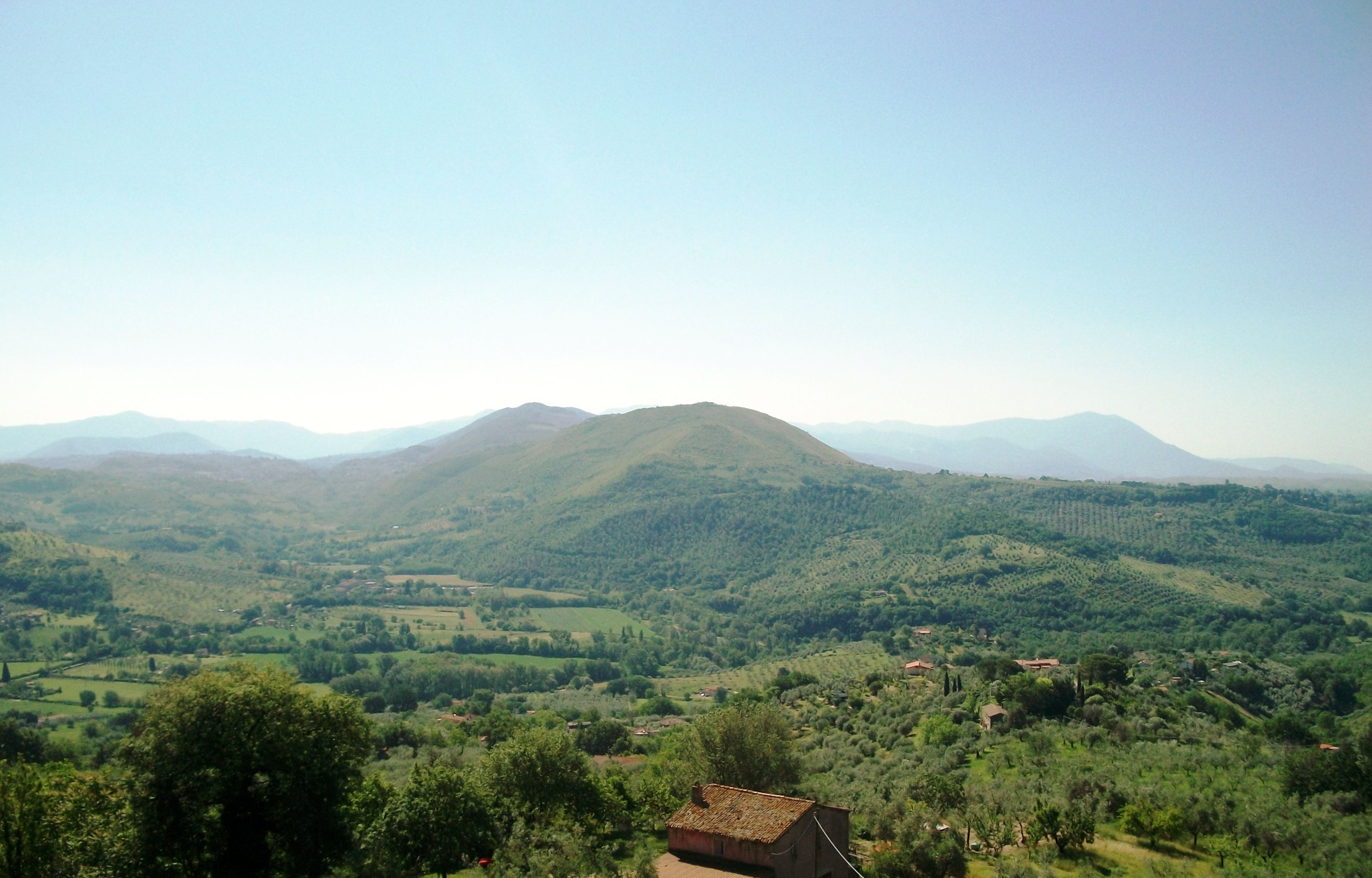 Un paysage rural caractérisé par des collines douces, des arbres dispersés et un petit bâtiment au premier plan.