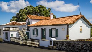 A traditional white building with a tiled roof, a stone wall, and a staircase leading to a balcony.