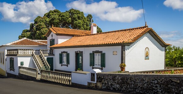 A traditional white building with a tiled roof, a stone wall, and a staircase leading to a balcony. - Vivenda Gomes (AL) - Traditional and comfortable house by the sea (Praia da Vitória)