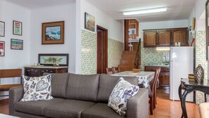 A living room with a sofa, a dining table, and a kitchen area with wooden cabinets and a refrigerator.