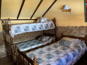 Un lit superposé avec une literie à carreaux, un mur en pierre et une lampe fixée au mur.