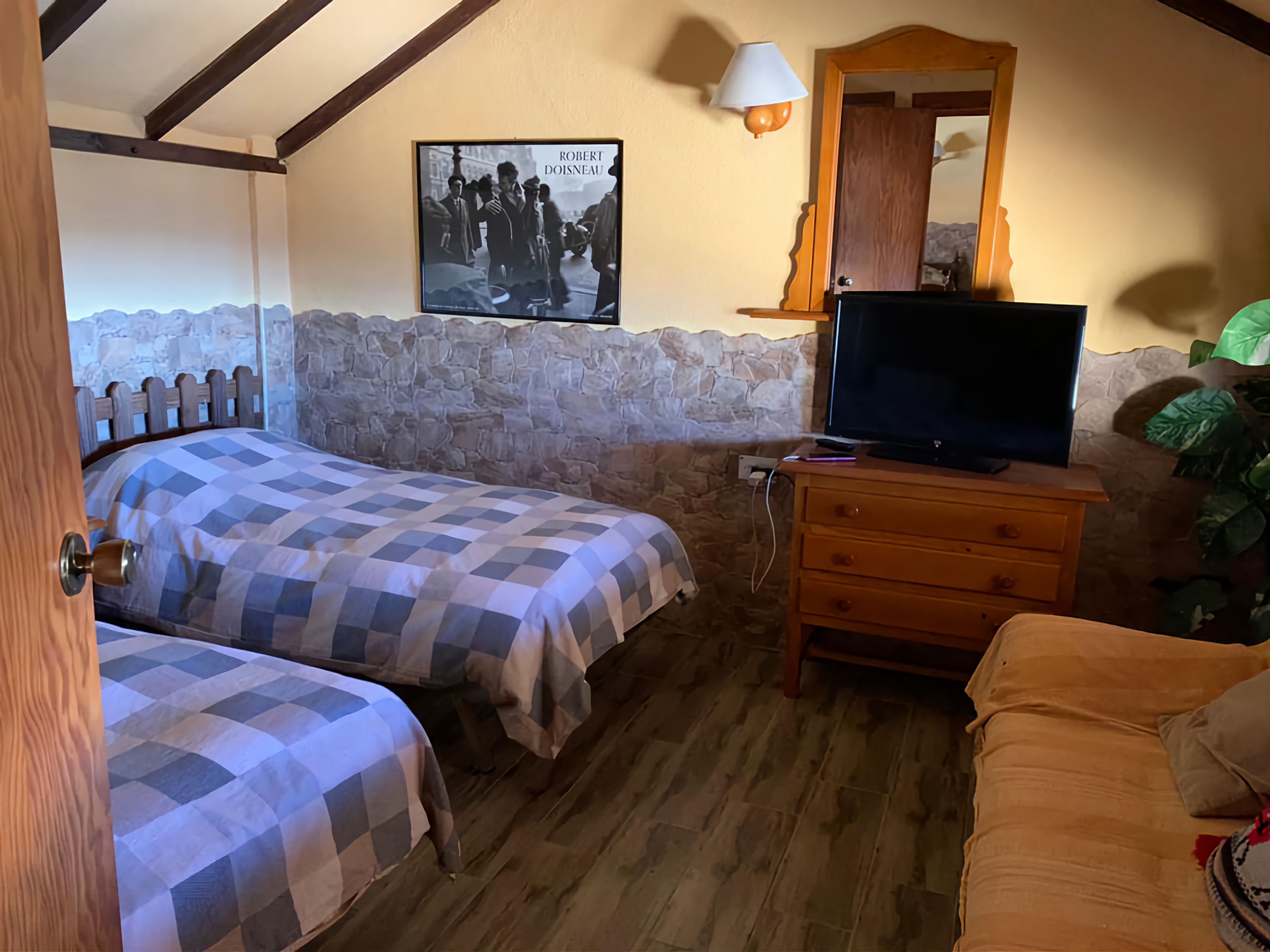 Een slaapkamer met twee bedden, een televisie op een houten dressoir, een stenen muur en een poster aan de wand.