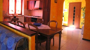 A dining area with a wooden table and chairs, a kitchen in the background, and a bright doorway leading to another room. - Casa Gabriella apartment with lake view (San Siro)