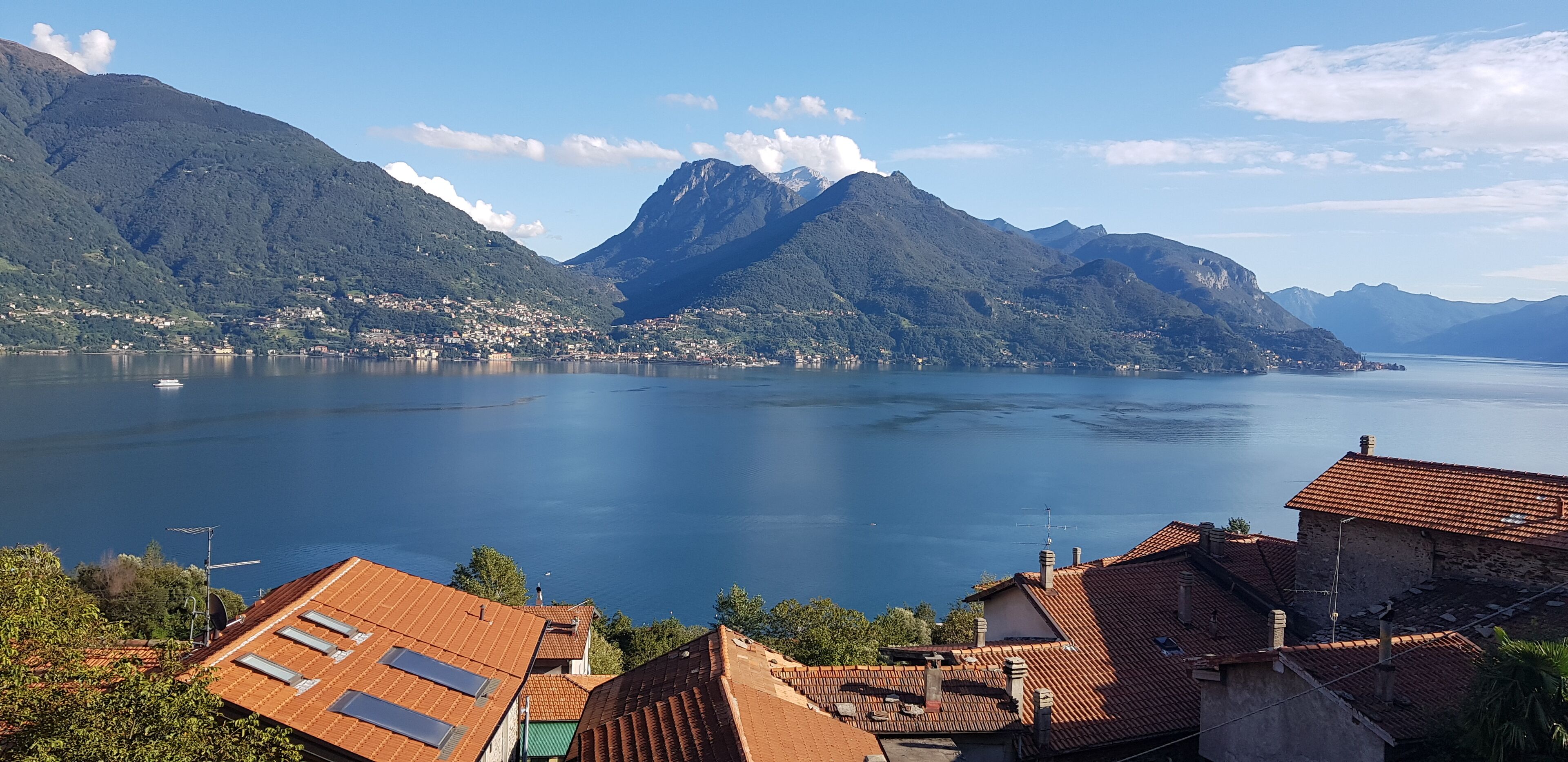 A coastal town with terracotta-roofed buildings, a large body of water, and mountains in the background.