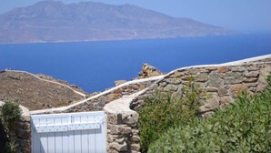 Un camino de piedra que lleva a una puerta blanca, con montañas al fondo y un mar azul despejado.