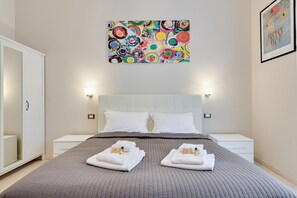 Une chambre d’hôtel moderne avec un grand lit, une tête de lit blanche et une peinture abstraite aux couleurs vives accrochée au-dessus.