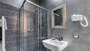 Casa de banho moderna com chuveiro em cabine de vidro, lavatório branco e secador de cabelo fixado na parede.