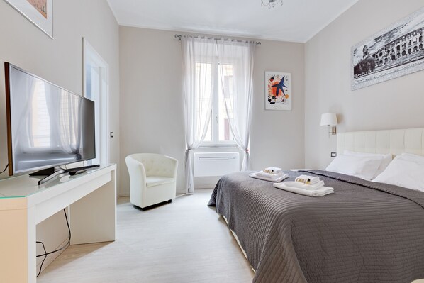 Une chambre d’hôtel avec un lit, une télévision, une chaise et une fenêtre avec des rideaux.