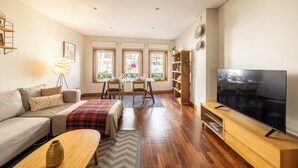 A living room with a sofa, coffee table, TV, wooden TV stand, dining table with chairs, and a bookshelf. - Spacious Downtown Apartment with Private Terrace (Porto)