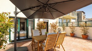 A patio with a table and chairs under a large umbrella, surrounded by potted plants and a view of buildings. - Spacious Downtown Apartment with Private Terrace (Porto)