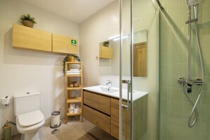 A modern bathroom with a toilet, sink, shower, and wooden shelving with towels. - Spacious Downtown Apartment with Private Terrace (Porto)