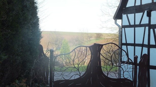 A gated entrance with a tree-like metal design, a stone pathway, and a building with exposed timber framing.