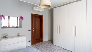 A bedroom with a wooden wardrobe, a white dresser, a mirror, and a hanging light fixture.