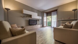 A modern living room with two sofas, a flat-screen TV, built-in shelving, and a sliding glass door leading to a balcony.