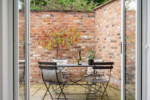 A patio with a brick wall, a table with chairs, a bottle, and a potted plant. - The Smithy - sleeps 2 guests  in 1 bedroom (York)