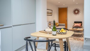 A modern kitchen with white cabinets, a dining table with chairs, a loaf of bread, a bottle of wine, and glasses.