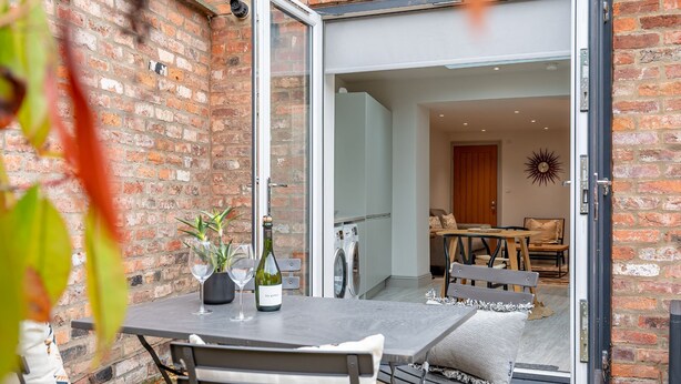 An outdoor patio with a table set for two, a bottle of wine, and a potted plant.