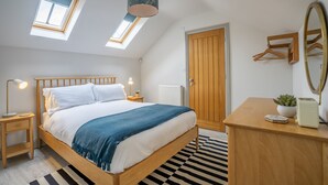 A bedroom with a wooden bed, skylights, a bedside table with a lamp, a dresser, a mirror, and a radiator.