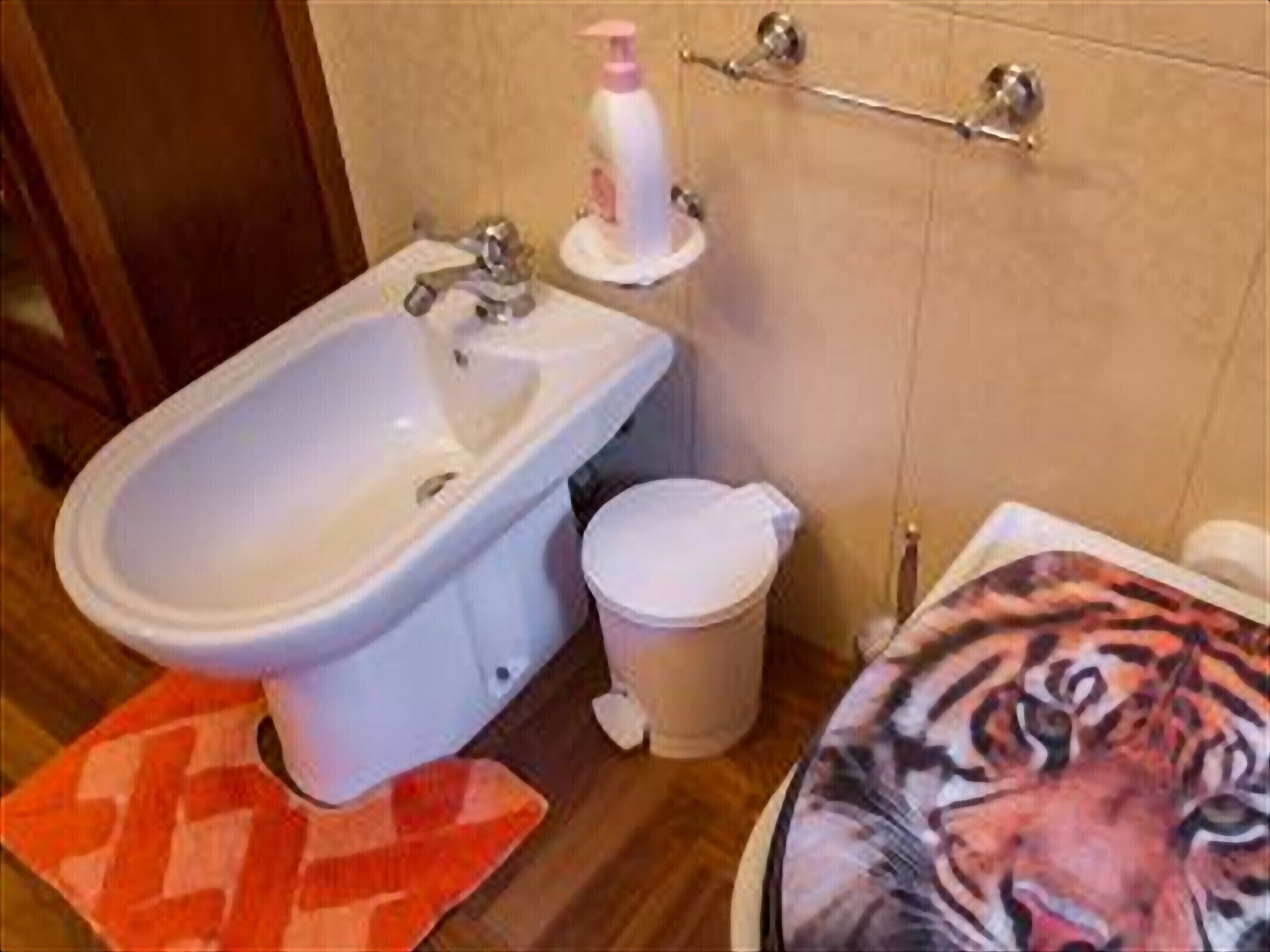 Un baño con un lavabo blanco, un inodoro y un bidé. Hay un perchero sobre el inodoro y un cubo de basura al lado.
